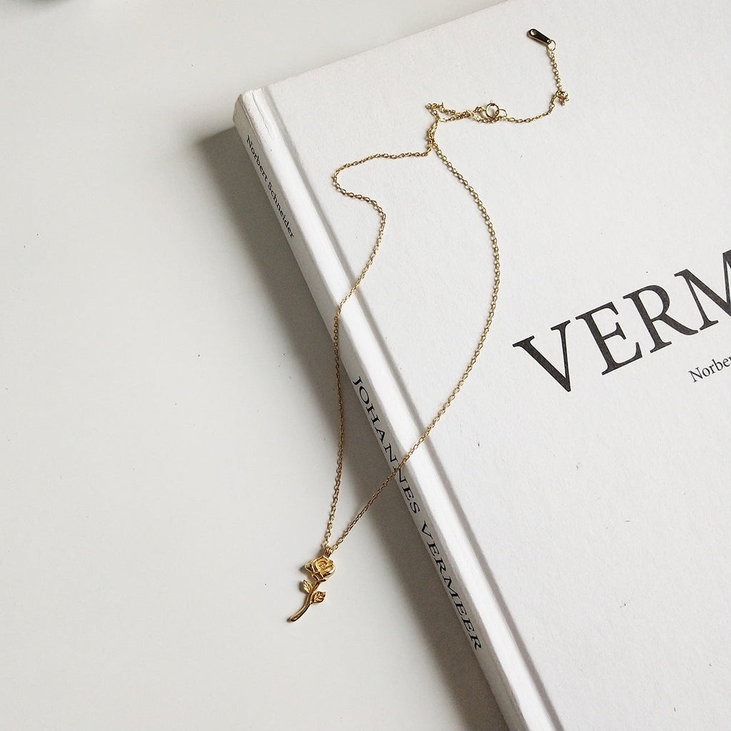 Lunéra de Paris gold-tone rose stem pendant necklace resting on a white art book