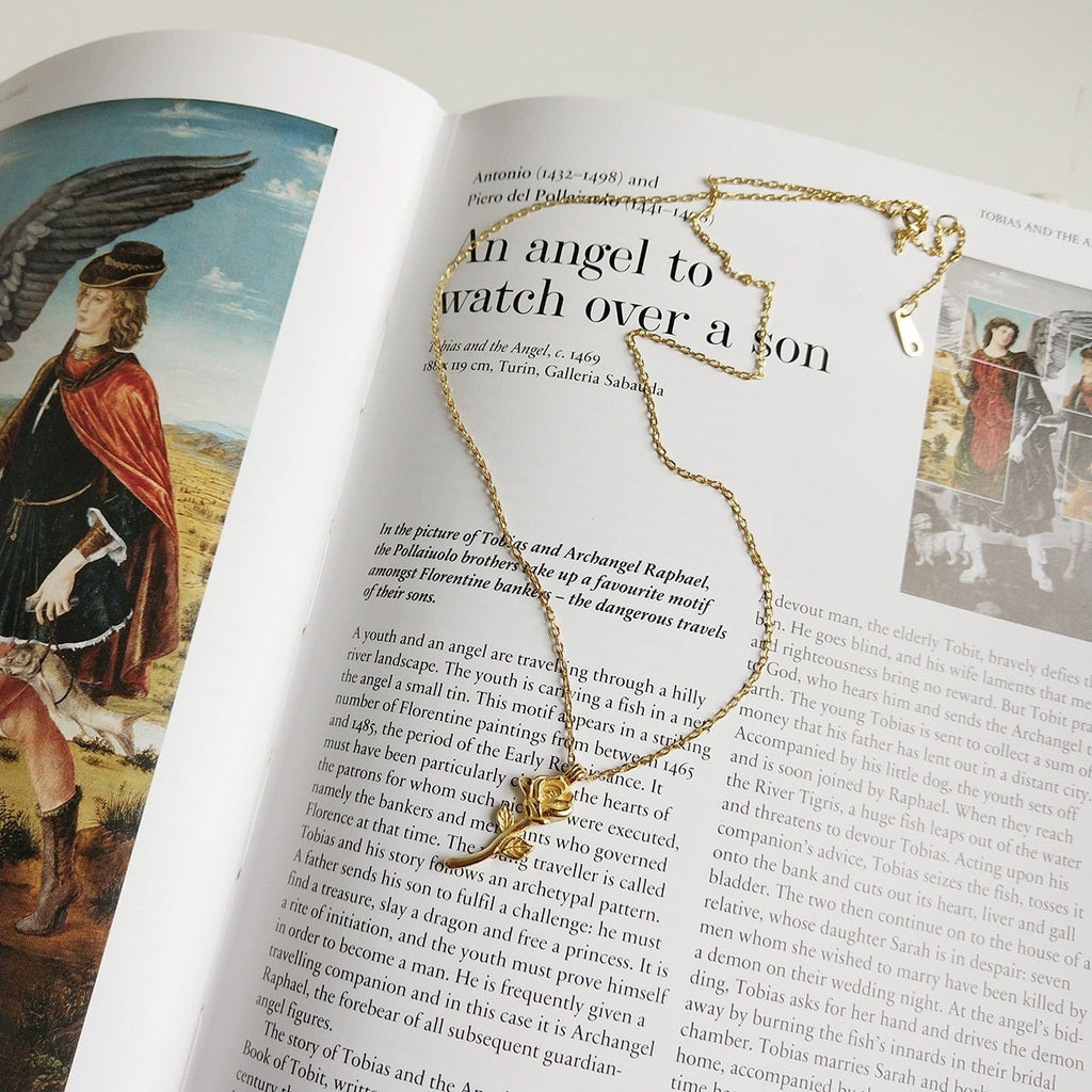 Lunéra de Paris gold-tone rose stem pendant necklace resting on an open art history book page