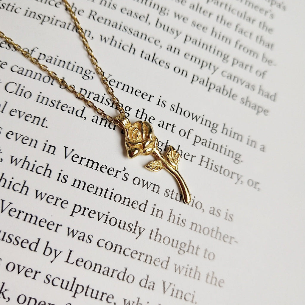 Lunéra de Paris gold-tone rose pendant necklace with stem and leaf detail resting on a page of a book