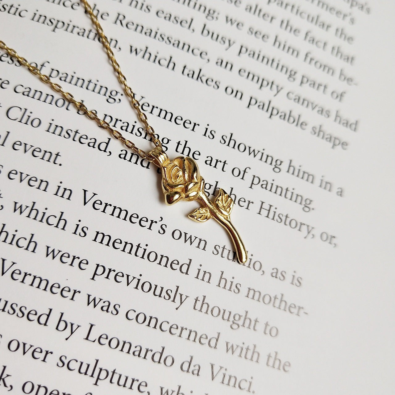 Lunéra de Paris gold-tone rose pendant necklace with stem and leaf detail resting on a page of a book