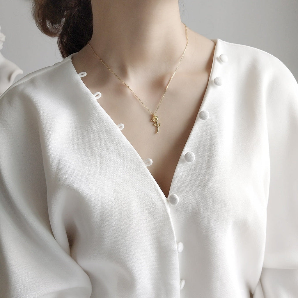 Lunéra de Paris gold-tone rose pendant necklace with stem and leaf detail worn on a model in a white button-up shirt