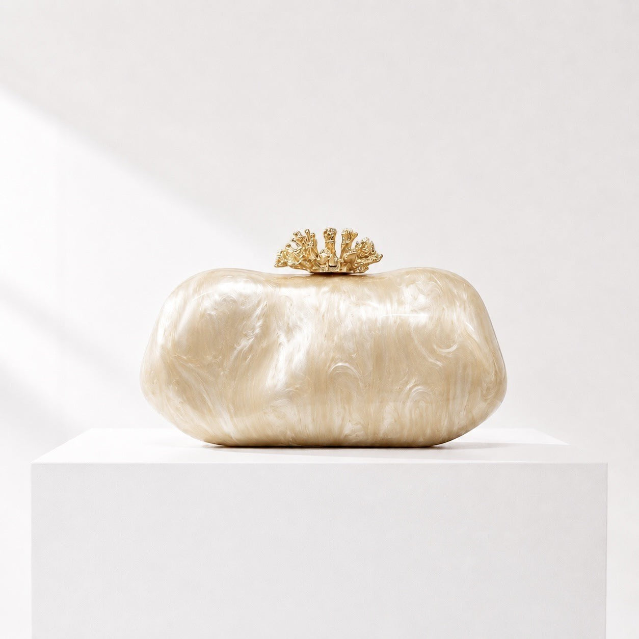 Lunéra de Paris oval acrylic clutch in a marbled champagne finish with a decorative gold-tone floral clasp