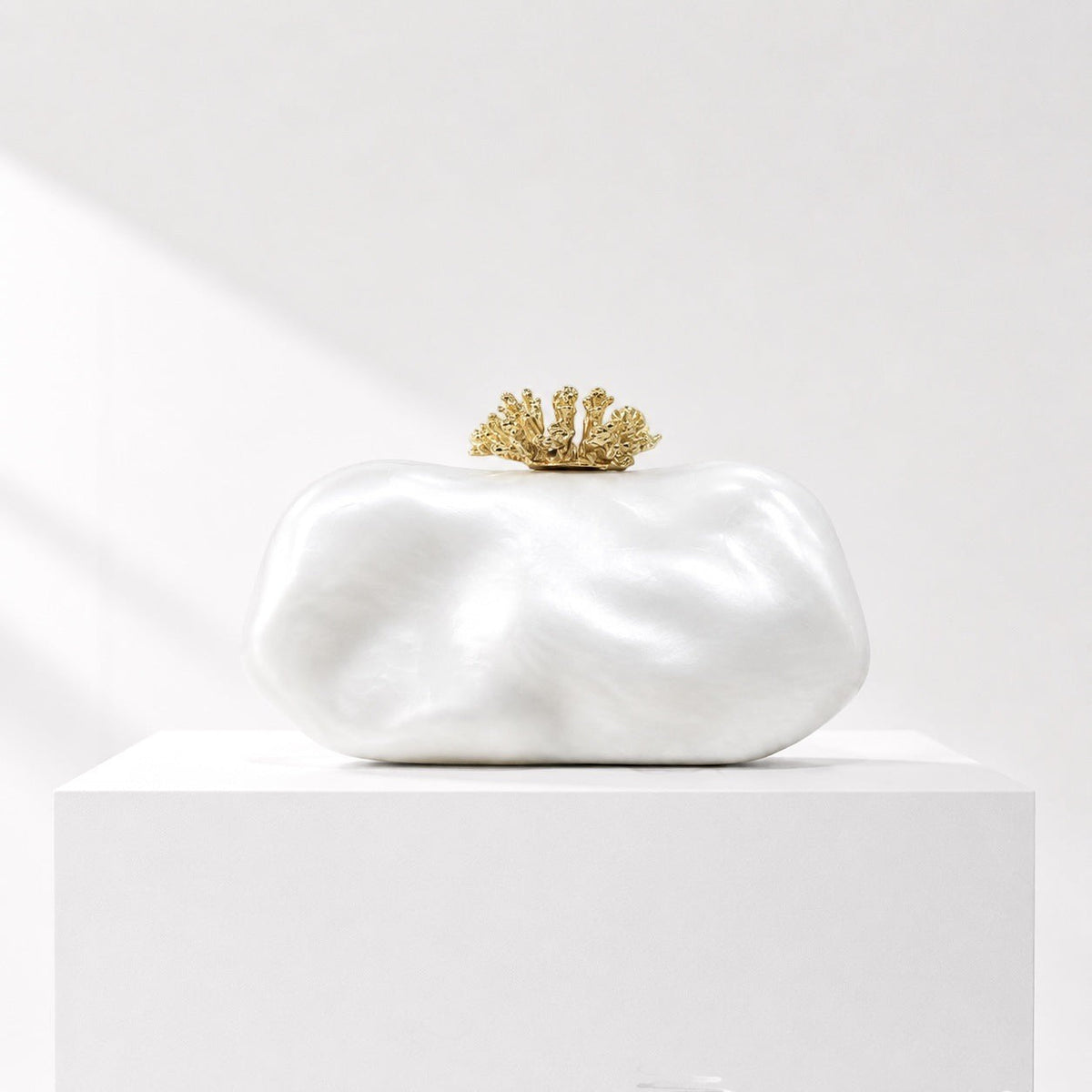 Lunéra de Paris white oval clutch bag with a decorative gold coral-inspired clasp on a white pedestal