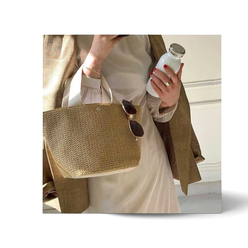 Lunéra de Paris Riviera woven beach bag with white handles held by a woman in a beige dress and blazer